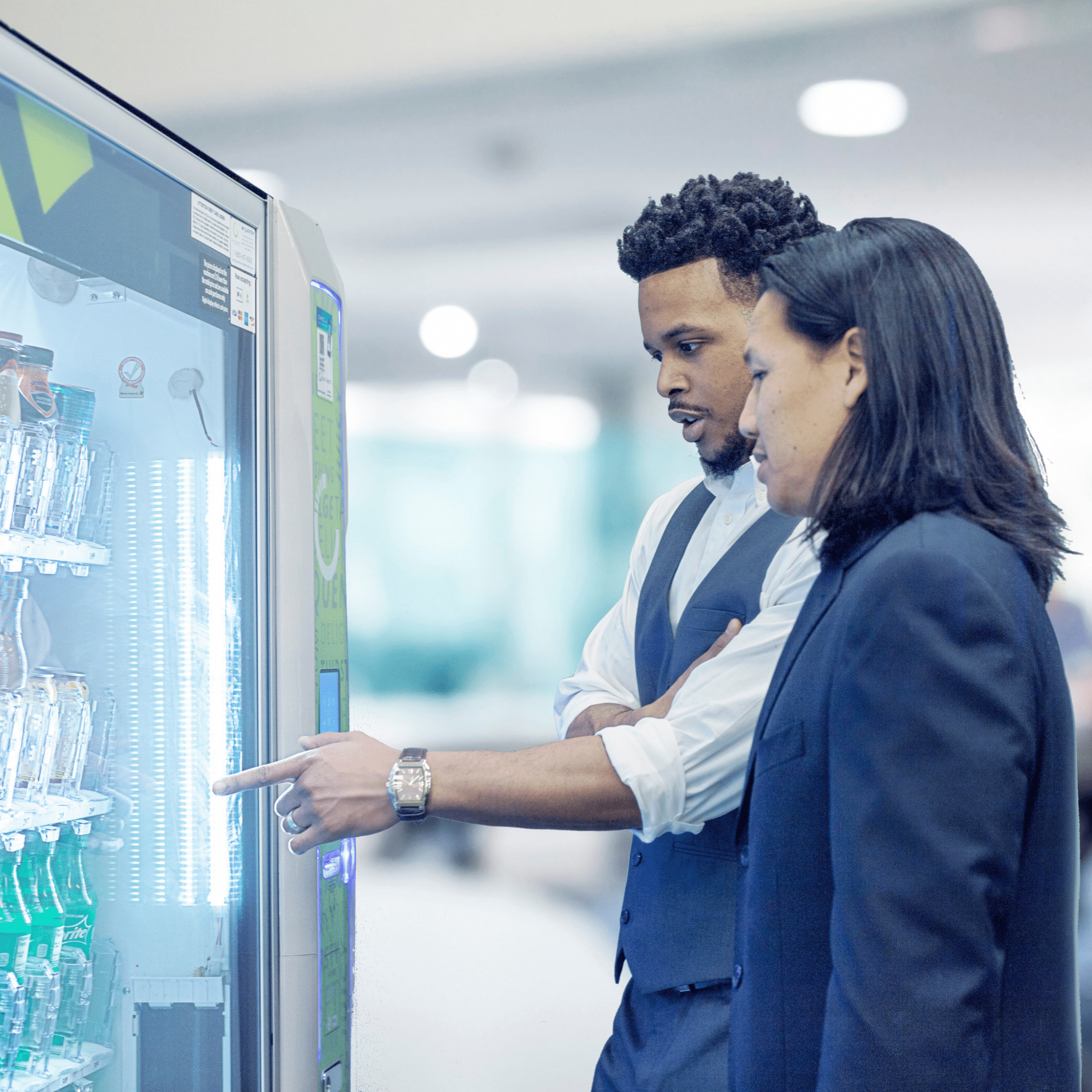 Two men looking at a vending machine and pointing to an option