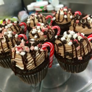 A plate of hot cocoa cupcakes with chocolate chips and candy cane garnish