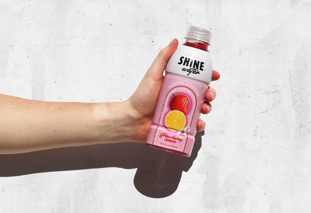 A hand holding a bottle of ShineWater Strawberry Lemon