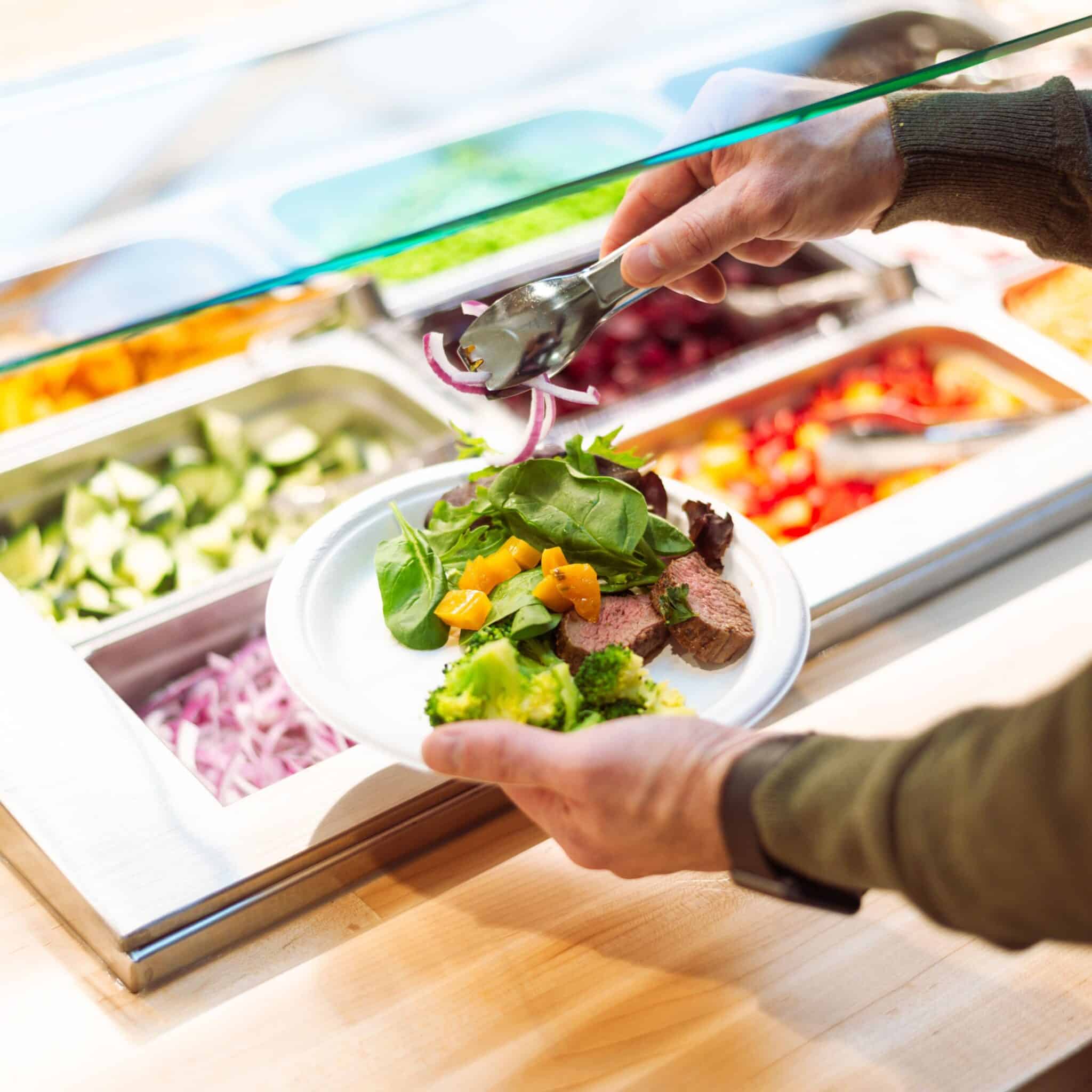 Buffet Style Dining Buffet-style dining area, person putting food on a plate, steak and salad