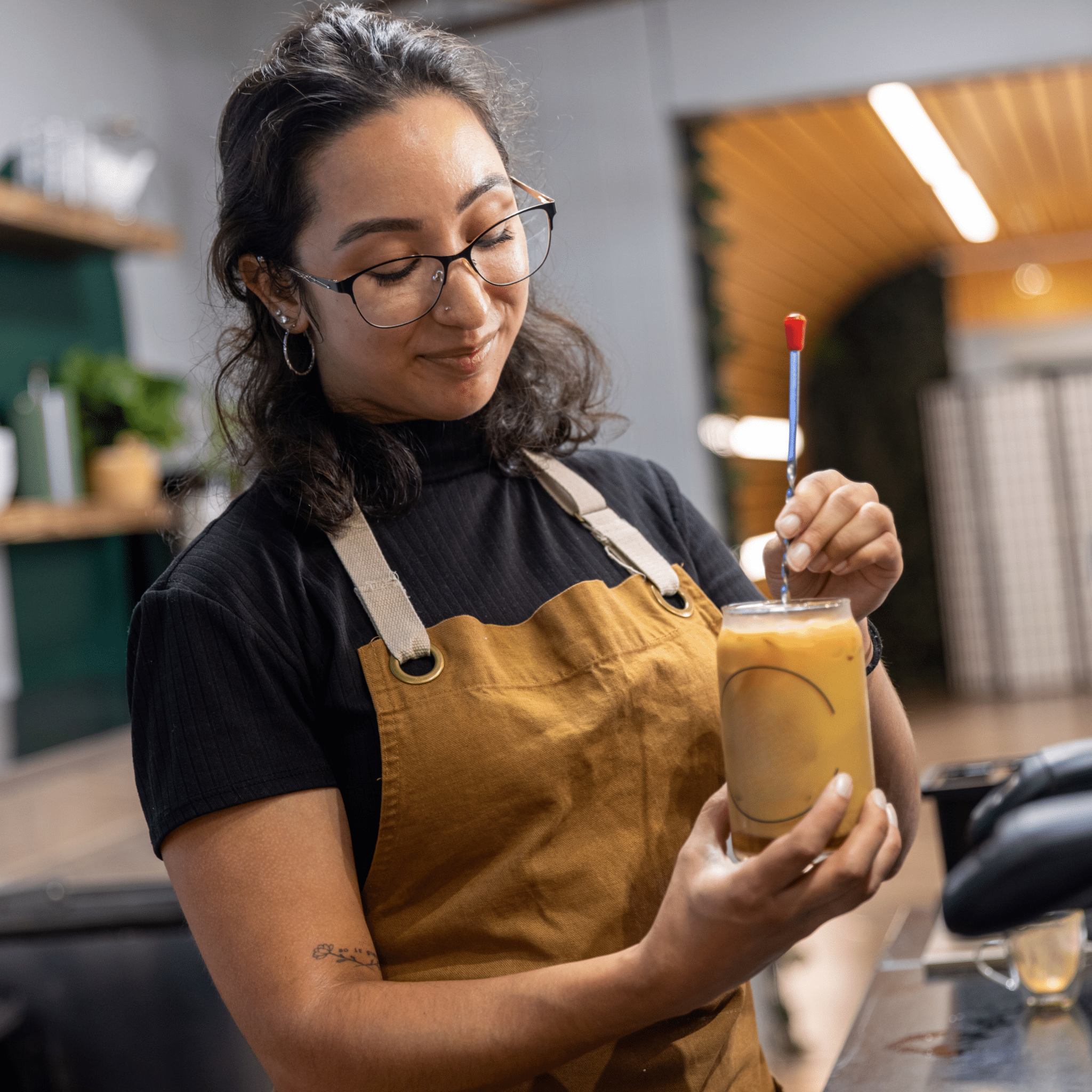 Barista stirring coffee in a glass cup, barista behind the bar, café