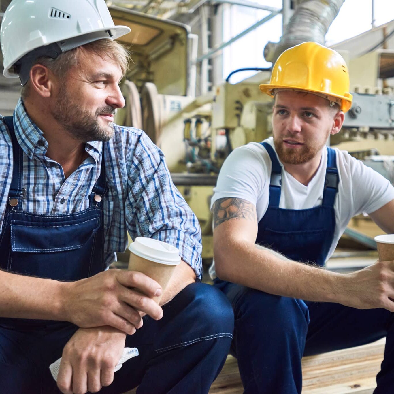 Two men in hard hats sitting and drinking coffee, manufacturing workers
